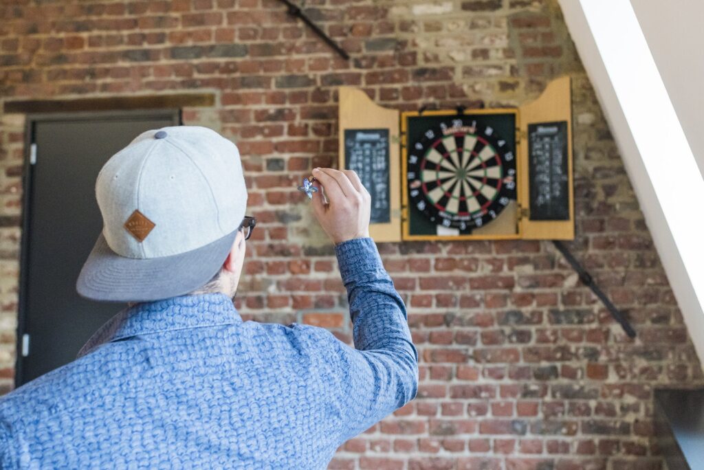 Back View Photo of Man in Blue Dress Shirt and Gray Hat Playing Darts